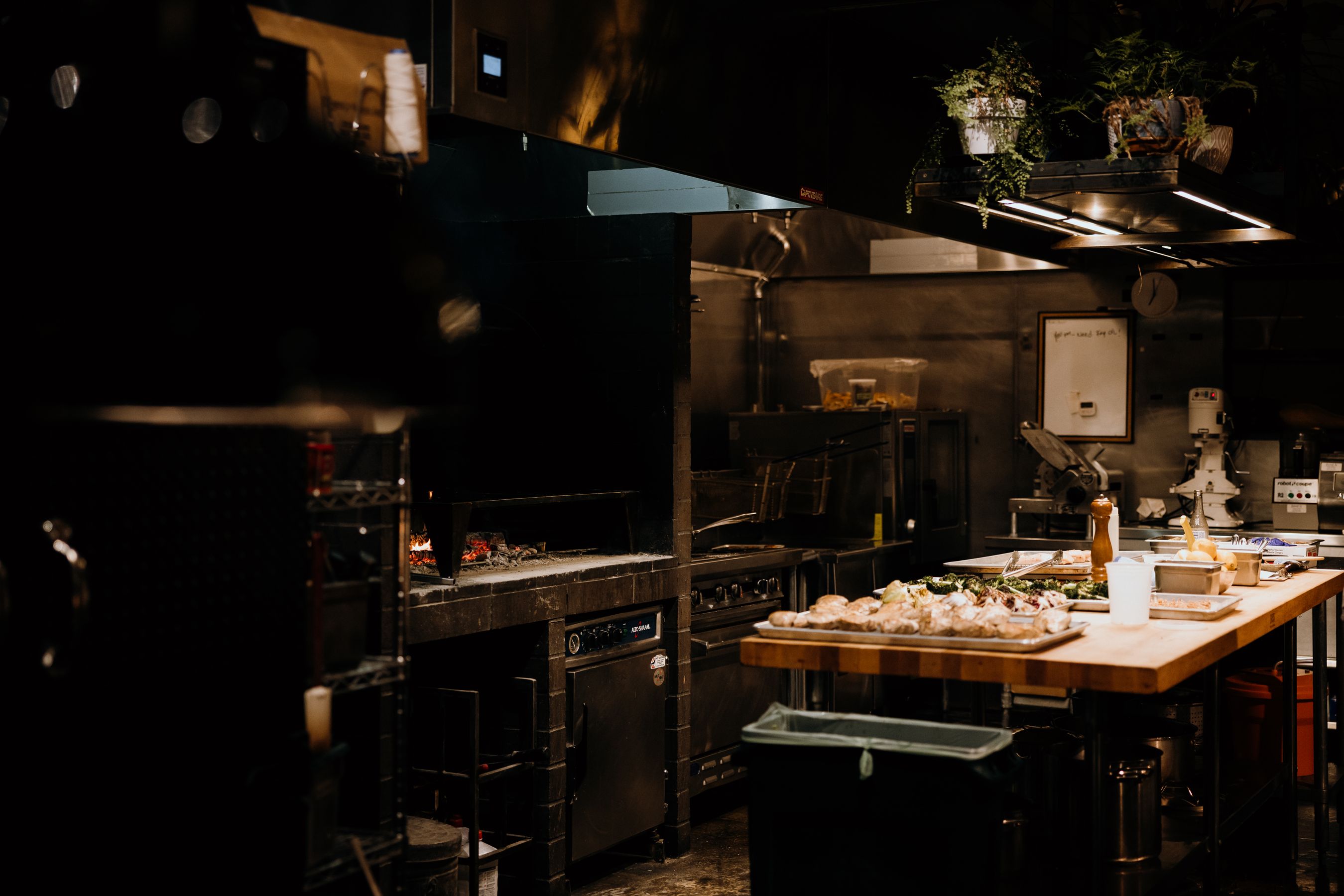 Warm working kitchen with cutting boards, whole ingredients laid out, late-afternoon light across wood — the room where sauces get made.