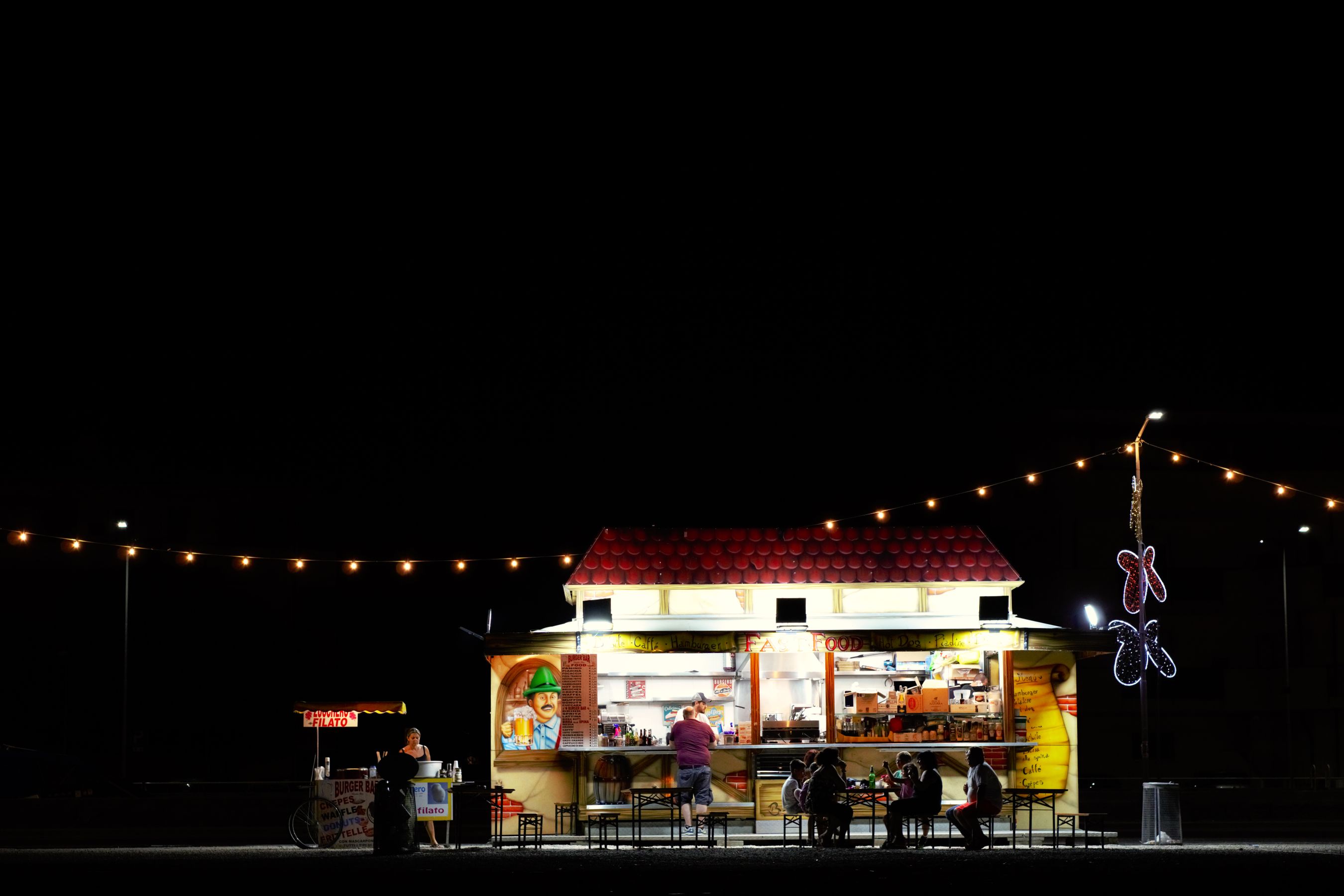 A night-market booth strung with warm bulb lights — the kind of setup the tent looks for when it lands somewhere.