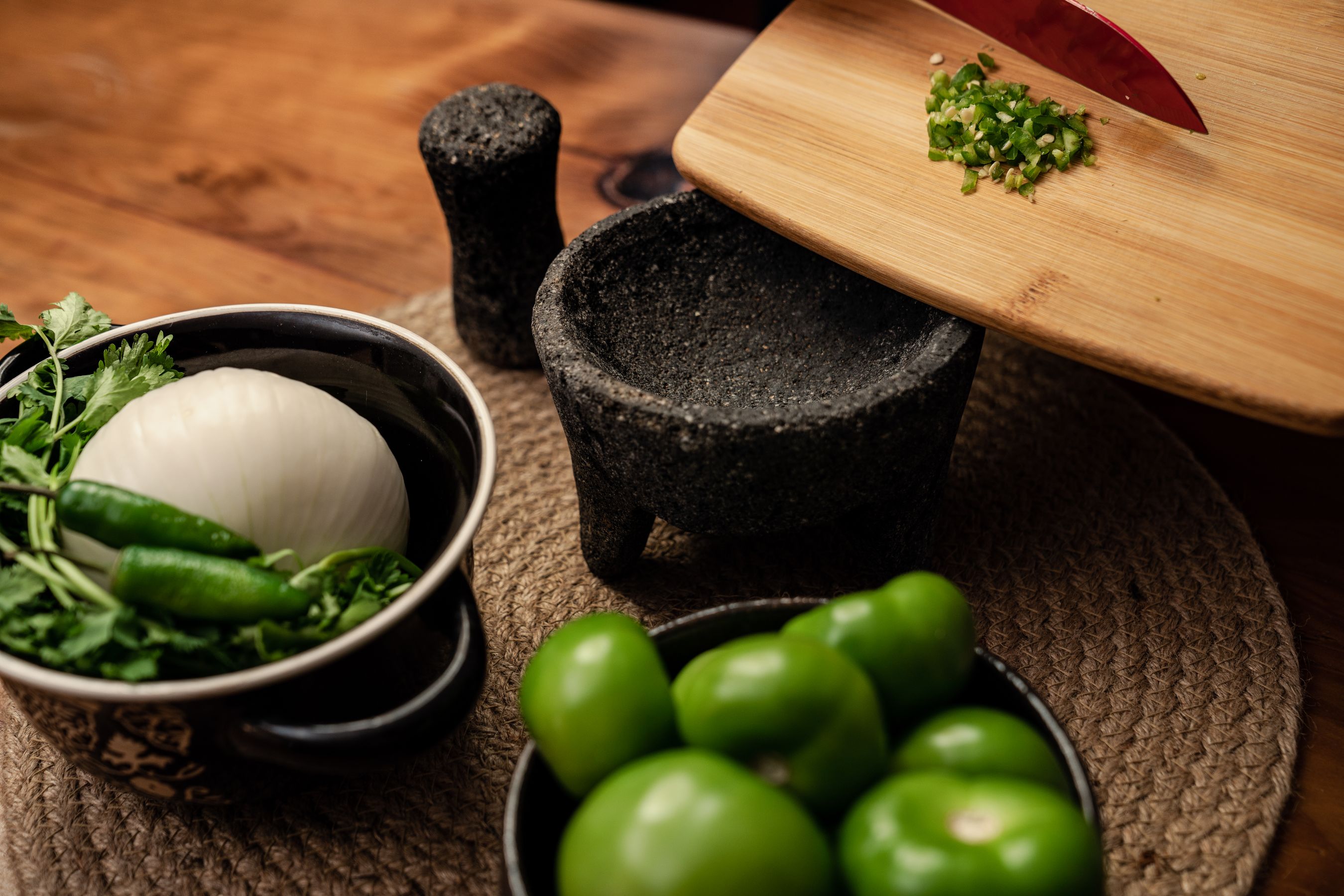 Fresh tomatillos, red onion, and cilantro on a rustic kitchen table — the ingredients before anything is done to them.